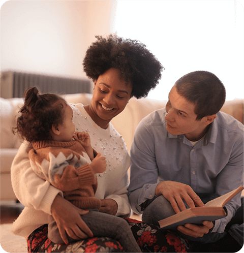 A woman and man holding a child while reading.